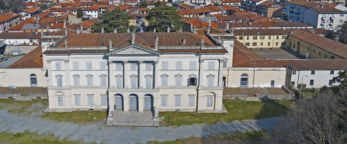 A large white building with a central entrance and statues on the roof, surrounded by red-roofed houses.