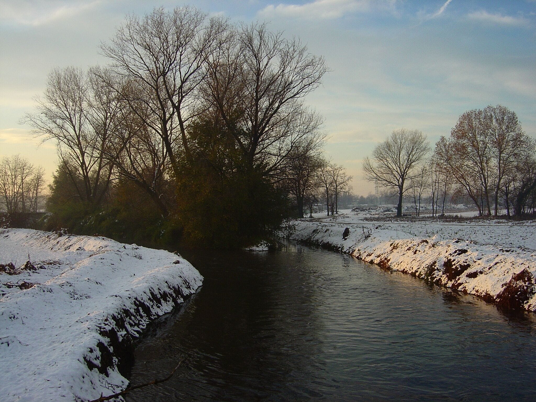 Un río cubierto de nieve con árboles desnudos y un cielo despejado.