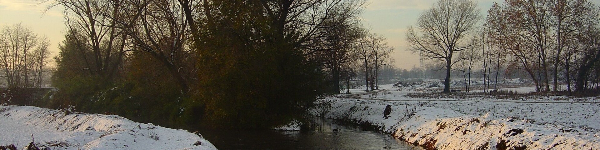 Un río cubierto de nieve con árboles desnudos y un cielo despejado.