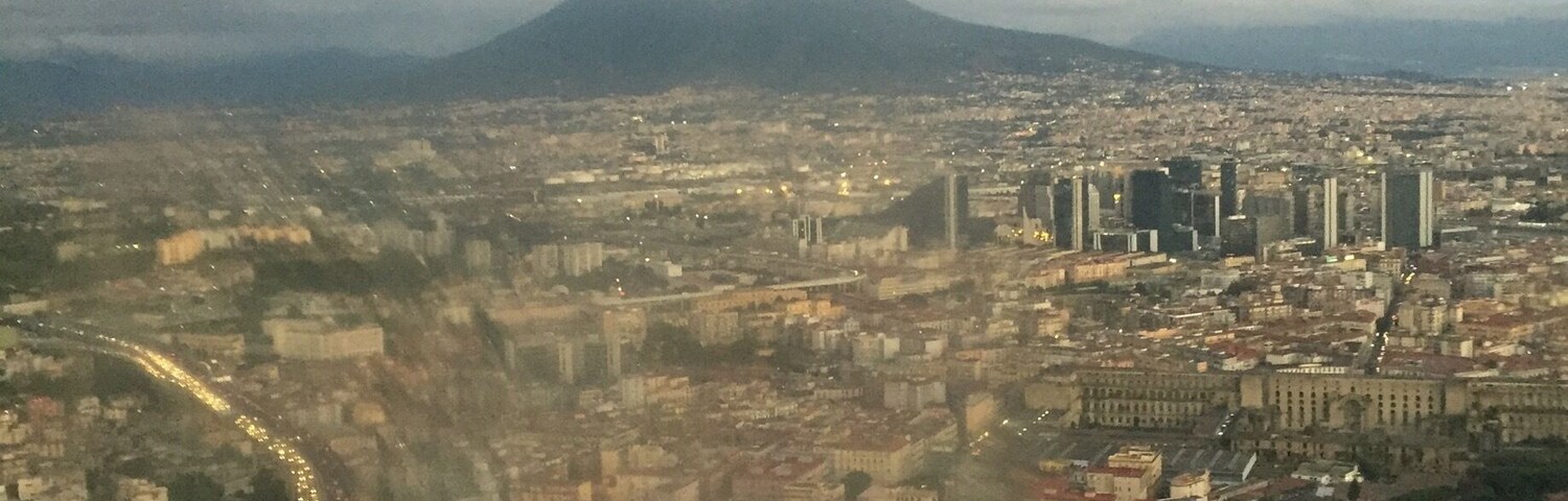 Un paysage urbain avec une montagne imposante en arrière-plan, une zone urbaine dense avec des bâtiments et une route sinueuse où circulent des véhicules.