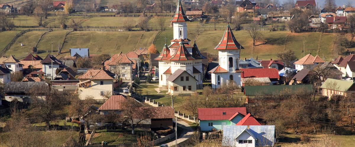 A village with a prominent church, surrounded by houses and rolling hills.