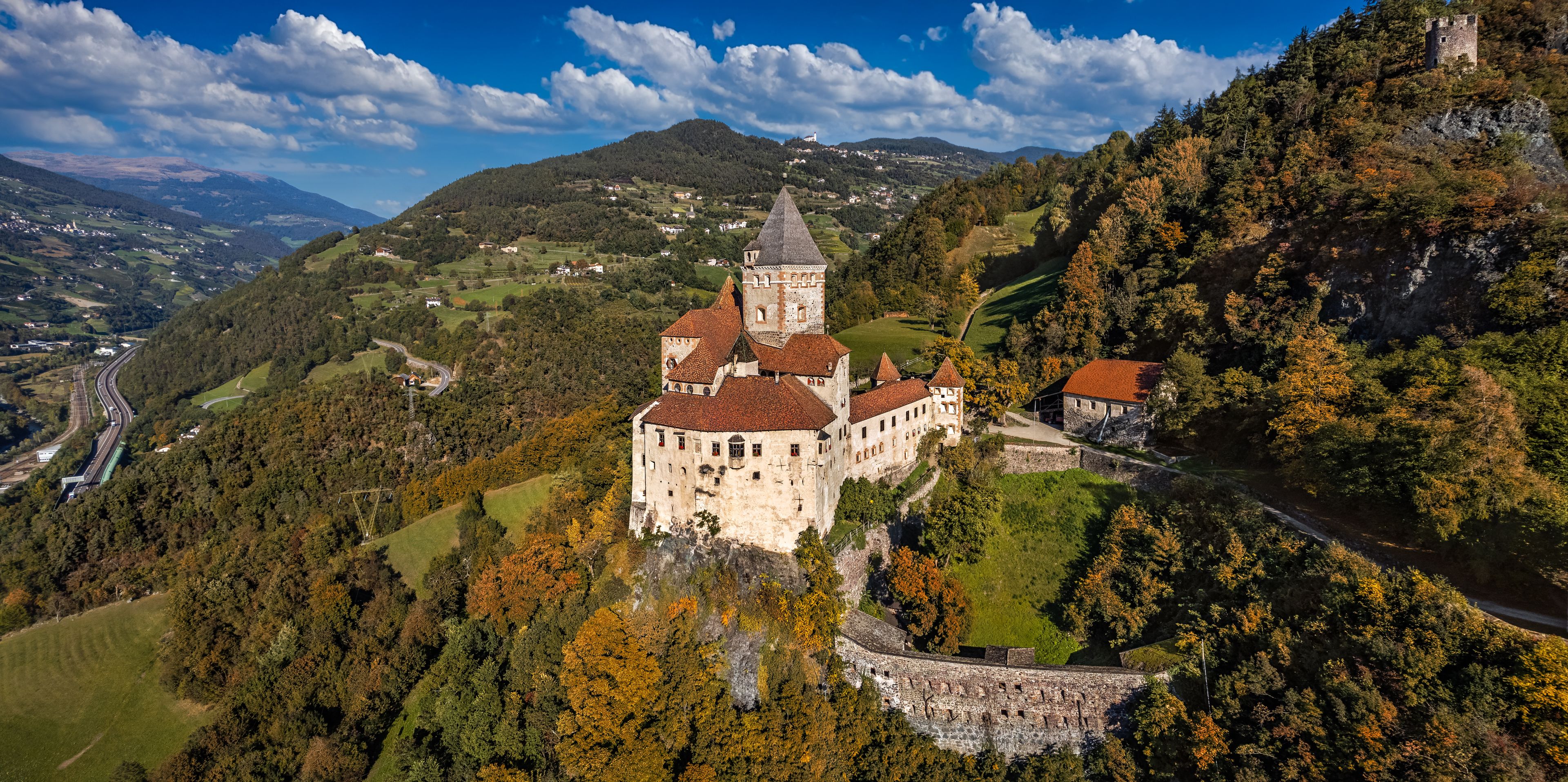 Val Isarco, Italy - Aerial panoramic view of Trostburg Castle (Castel Trostburg), a XII century fortress at the Italian Dolomites on a sunny autumn day with autumn foliage and blue sky with clouds