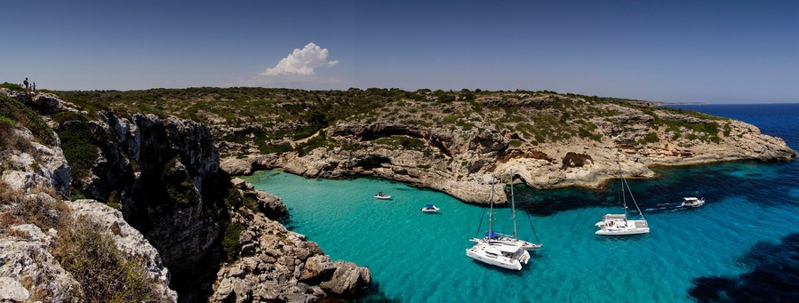 Paisaje costero con acantilados rocosos, aguas turquesas cristalinas y varios barcos anclados.