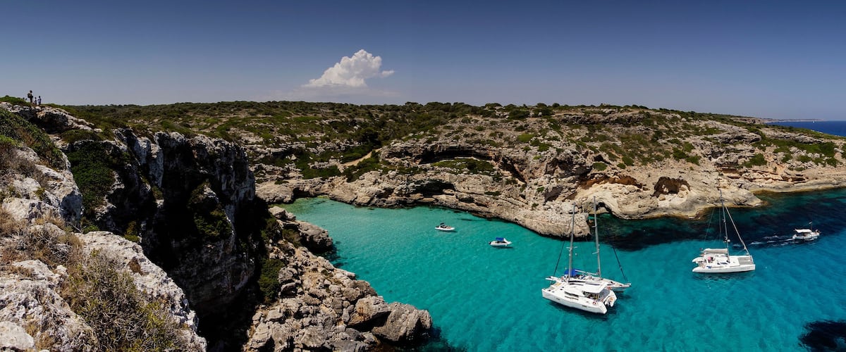 A coastal landscape with rocky cliffs, clear turquoise waters, and several anchored boats.