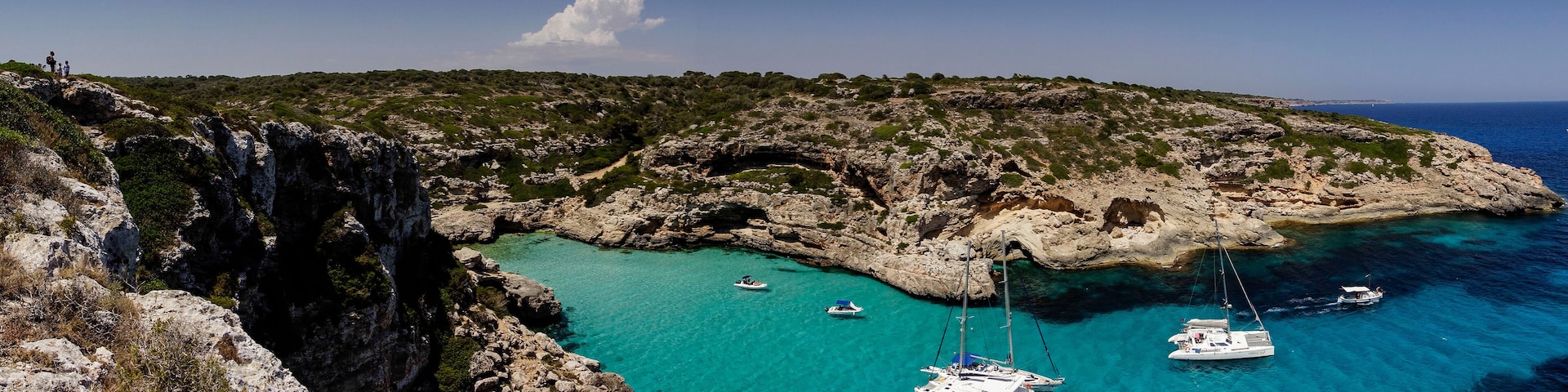 A coastal landscape with rocky cliffs, clear turquoise waters, and several anchored boats.