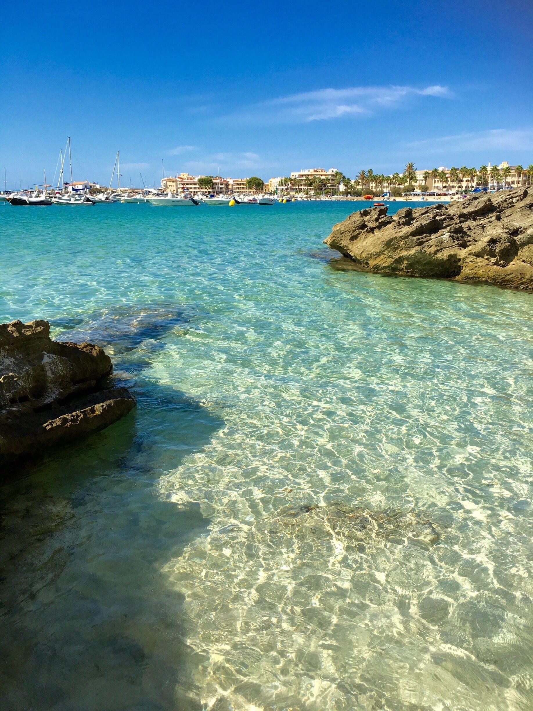 A clear coastal waterscape with rocky formations and a marina in the background.