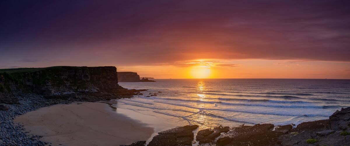 A sunset over a beach with rocky cliffs.