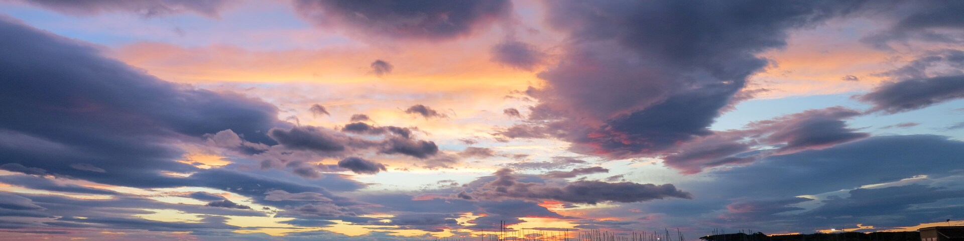 A sunset over a calm sea with a pier extending into the water, surrounded by a rocky coastline.