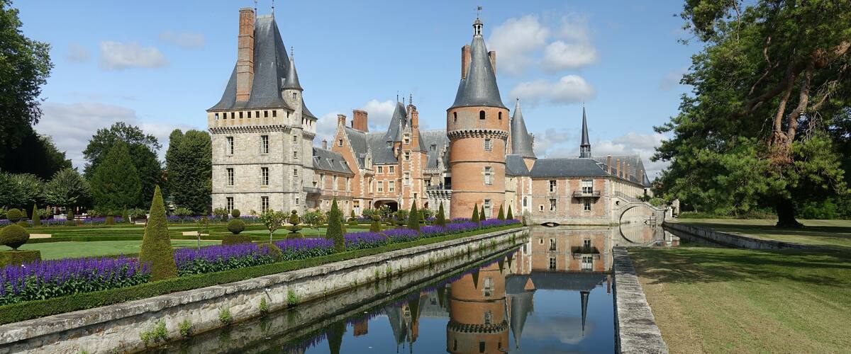 A historic castle with multiple towers and a reflective water canal.