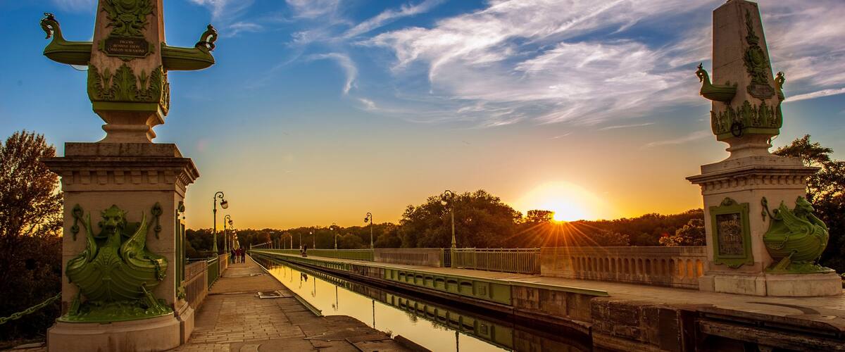A canal with a bridge, statues, and a sunset.
