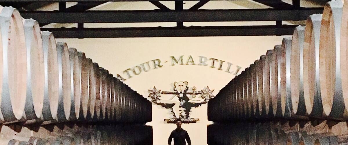 A person walking through a tunnel of wine barrels with a sign reading "ATOUR-MARTIN" above.