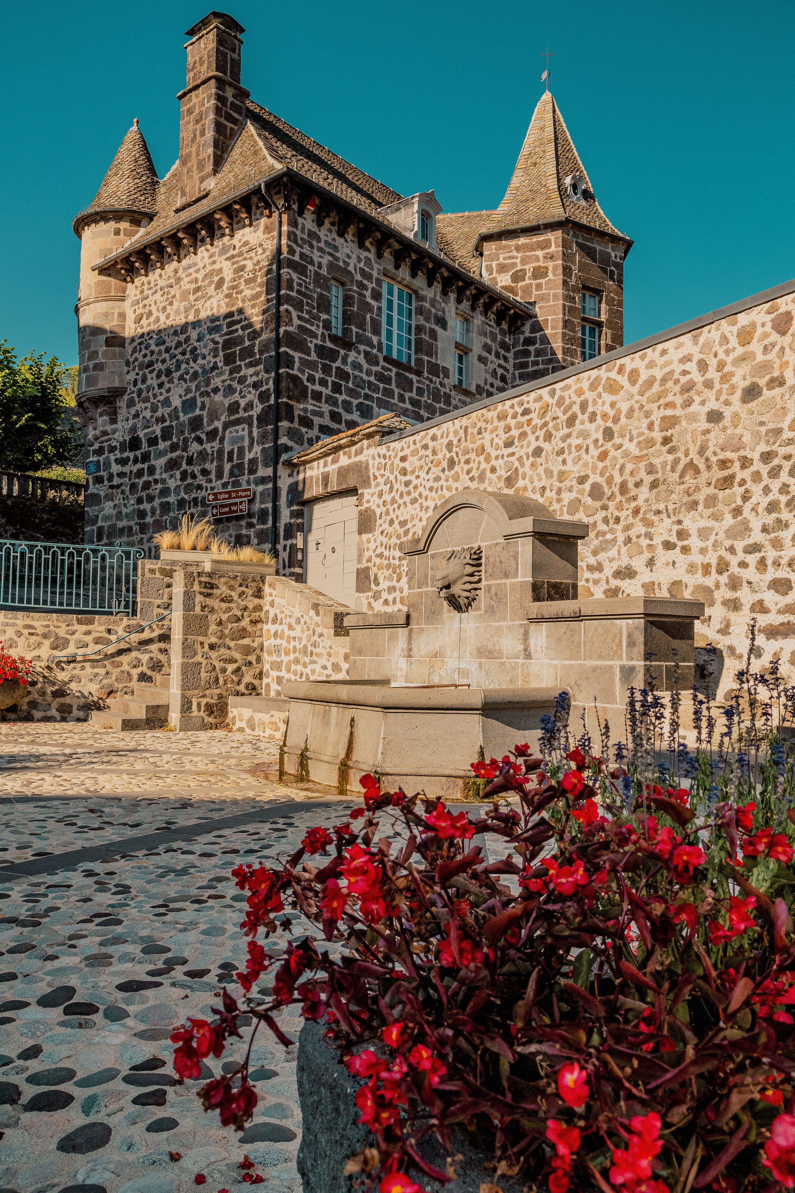 A historic stone building with a clock tower and a stone wall with a gate.