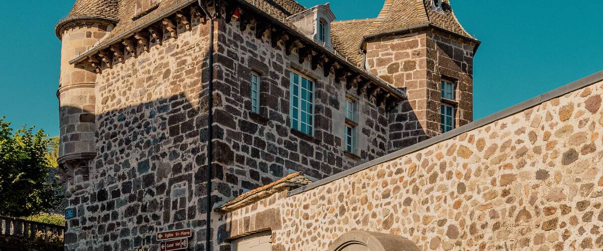 A historic stone building with a clock tower and a stone wall with a gate.