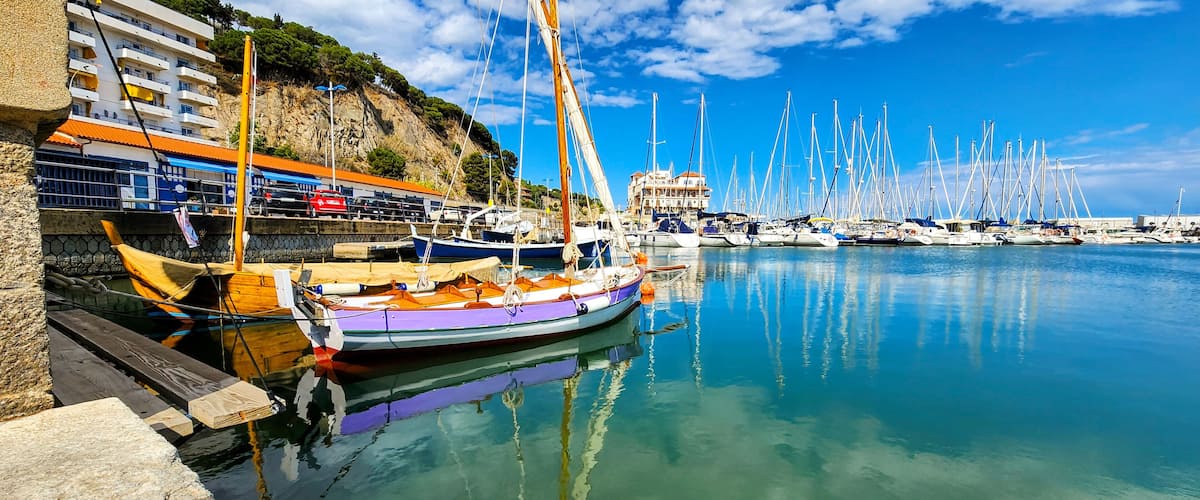 A marina with boats docked, a cliff with buildings, and a clear blue sky.