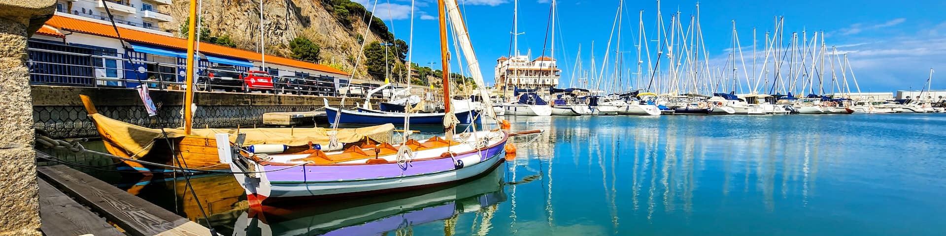A marina with boats docked, a cliff with buildings, and a clear blue sky.