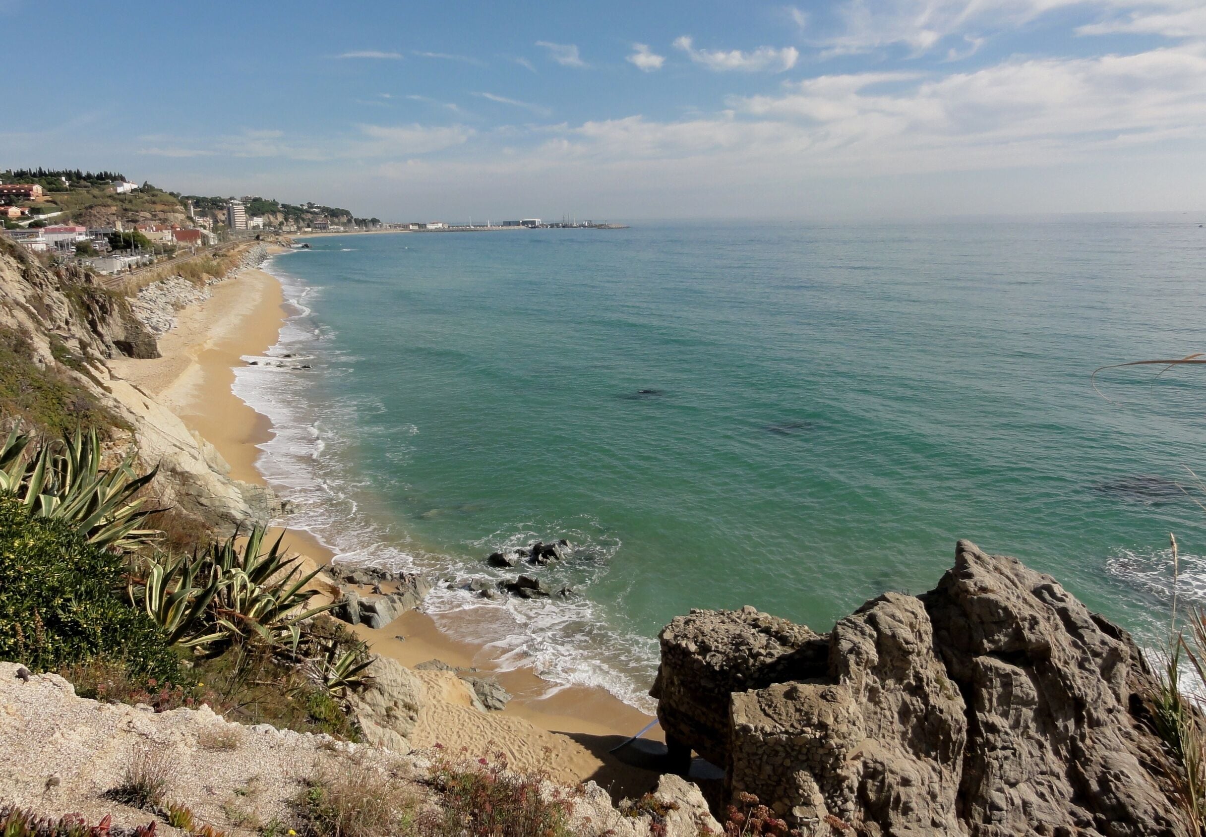 A coastal landscape with a sandy beach, rocky cliffs, and a clear blue sea.
