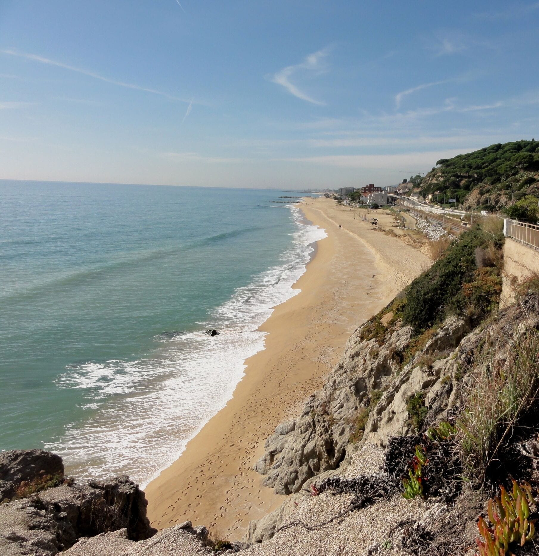 A coastal landscape with a sandy beach, rocky cliffs, and a clear blue sky.