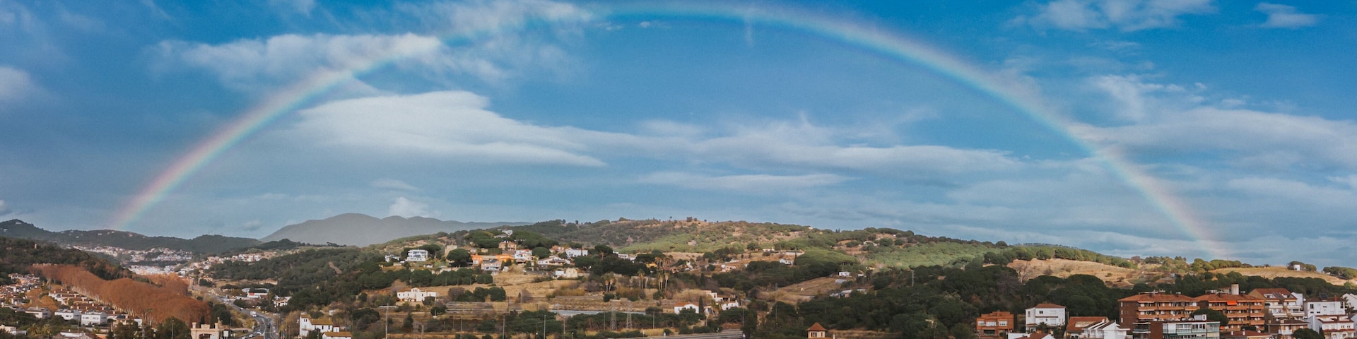 Un paisaje urbano con un arcoíris sobre un puente y colinas al fondo.
