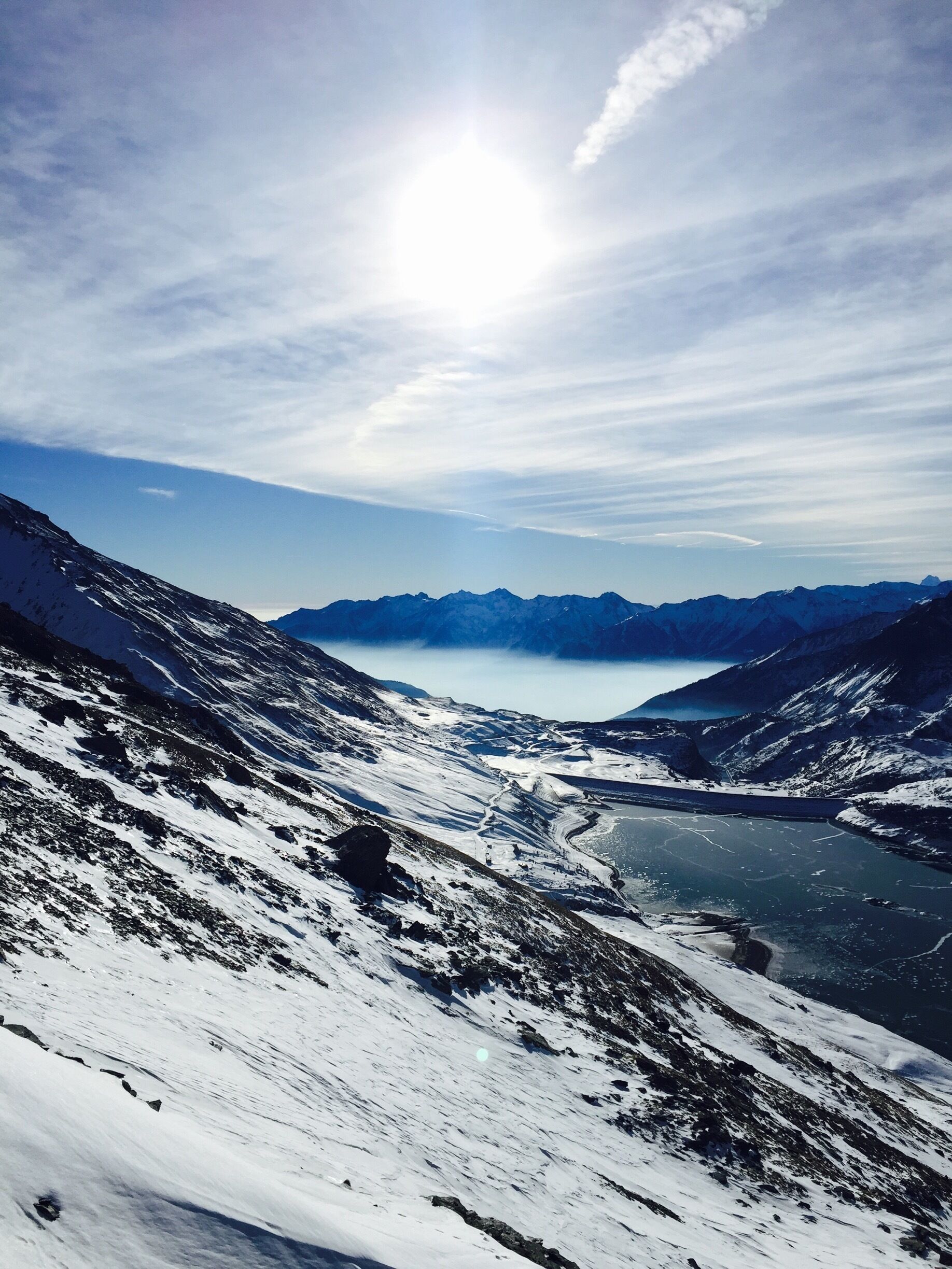A snow-covered mountain landscape with a lake and distant mountains under a clear sky.