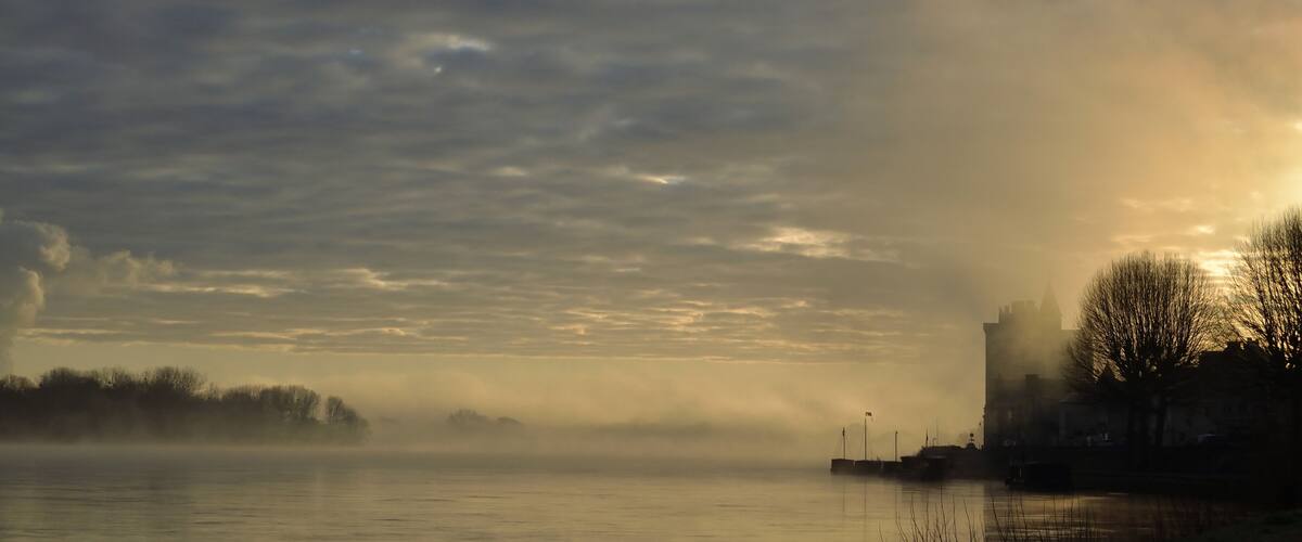 A river with a misty landscape, a distant city skyline, and a few boats.