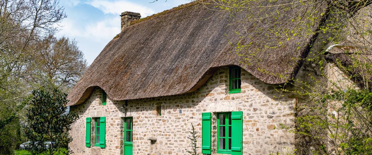 A stone house with a thatched roof and green shutters.