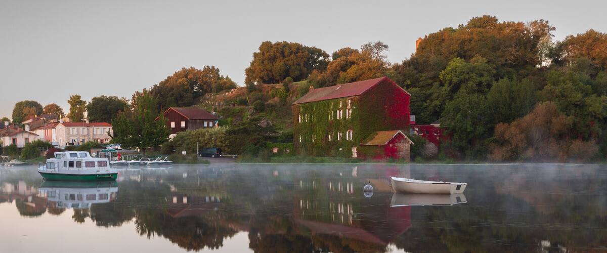 A calm lake with a green boat, a white boat, and a red building with ivy.