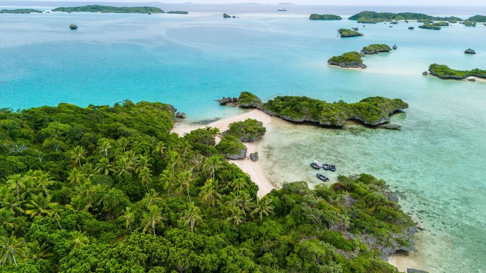 A tropical island with clear turquoise waters, lush green vegetation, and small rocky outcrops.