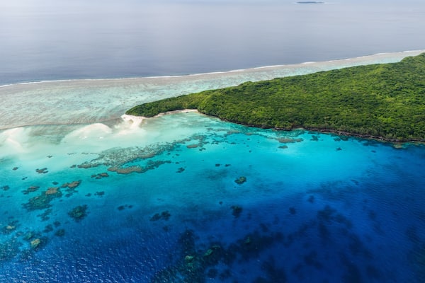 A tropical island with clear turquoise waters, a sandy beach, and dense green vegetation.