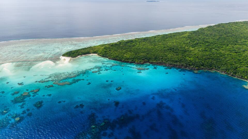 A tropical island with clear turquoise waters, a sandy beach, and dense green vegetation.