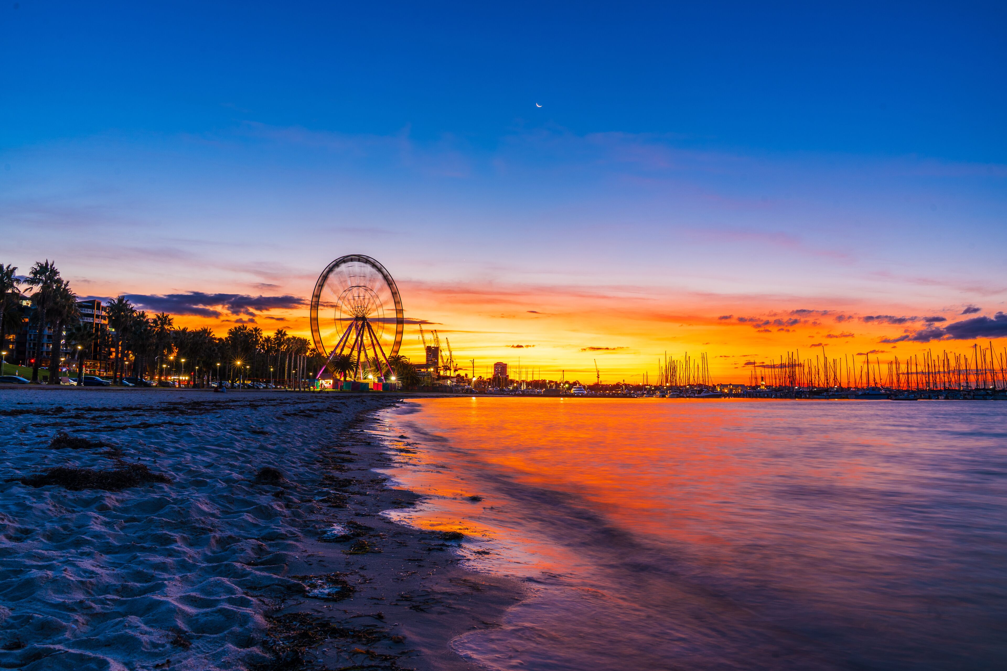 A beach at sunset with a Ferris wheel and a city skyline in the background.