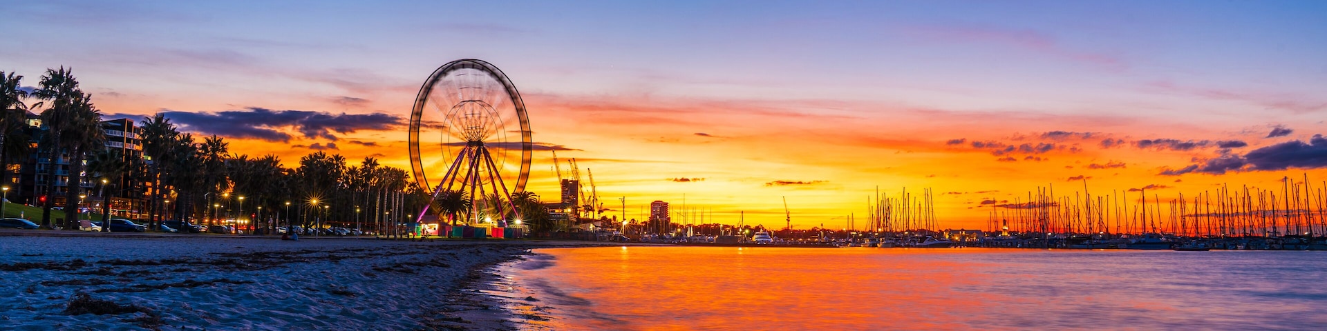 Una playa al atardecer con una noria y el perfil urbano del horizonte.