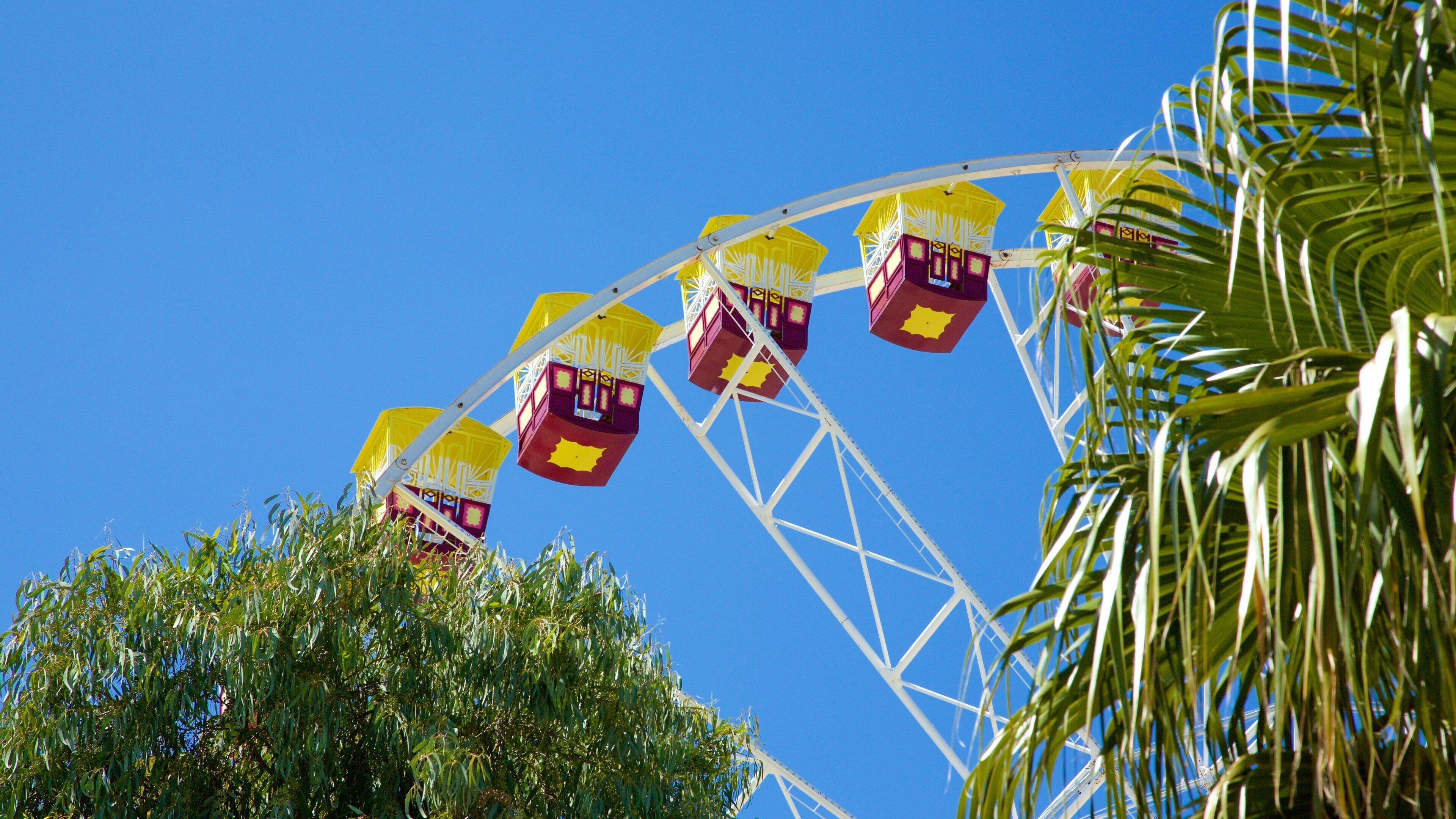 A Ferris wheel with yellow and purple gondolas against a clear blue sky.