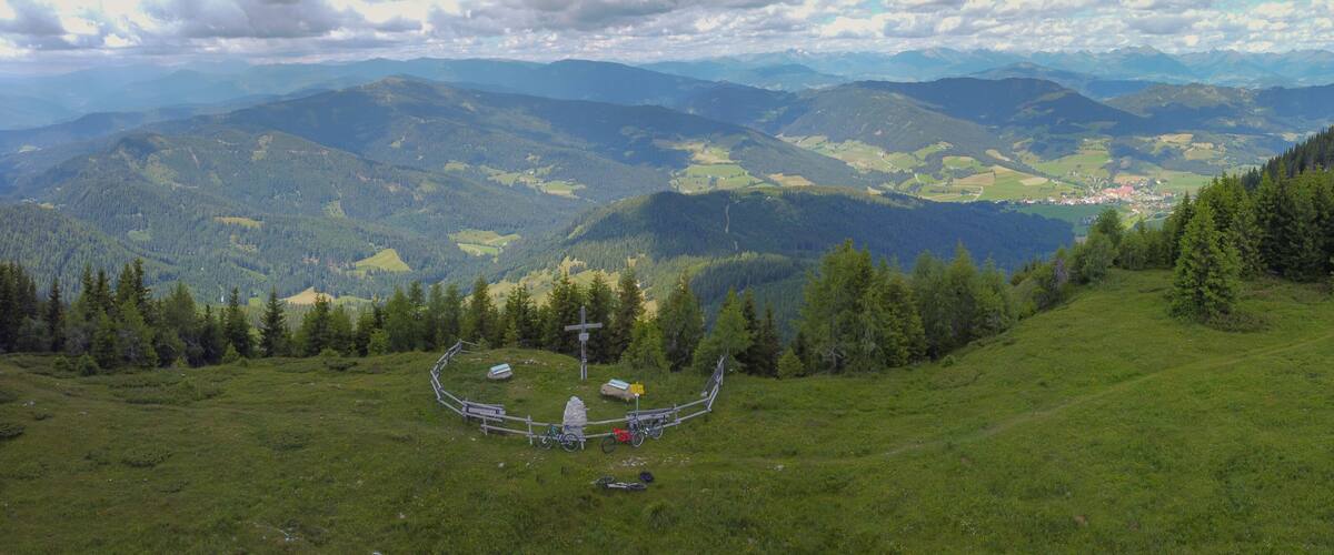 A mountainous landscape with a fenced area, a cross, and a small building.