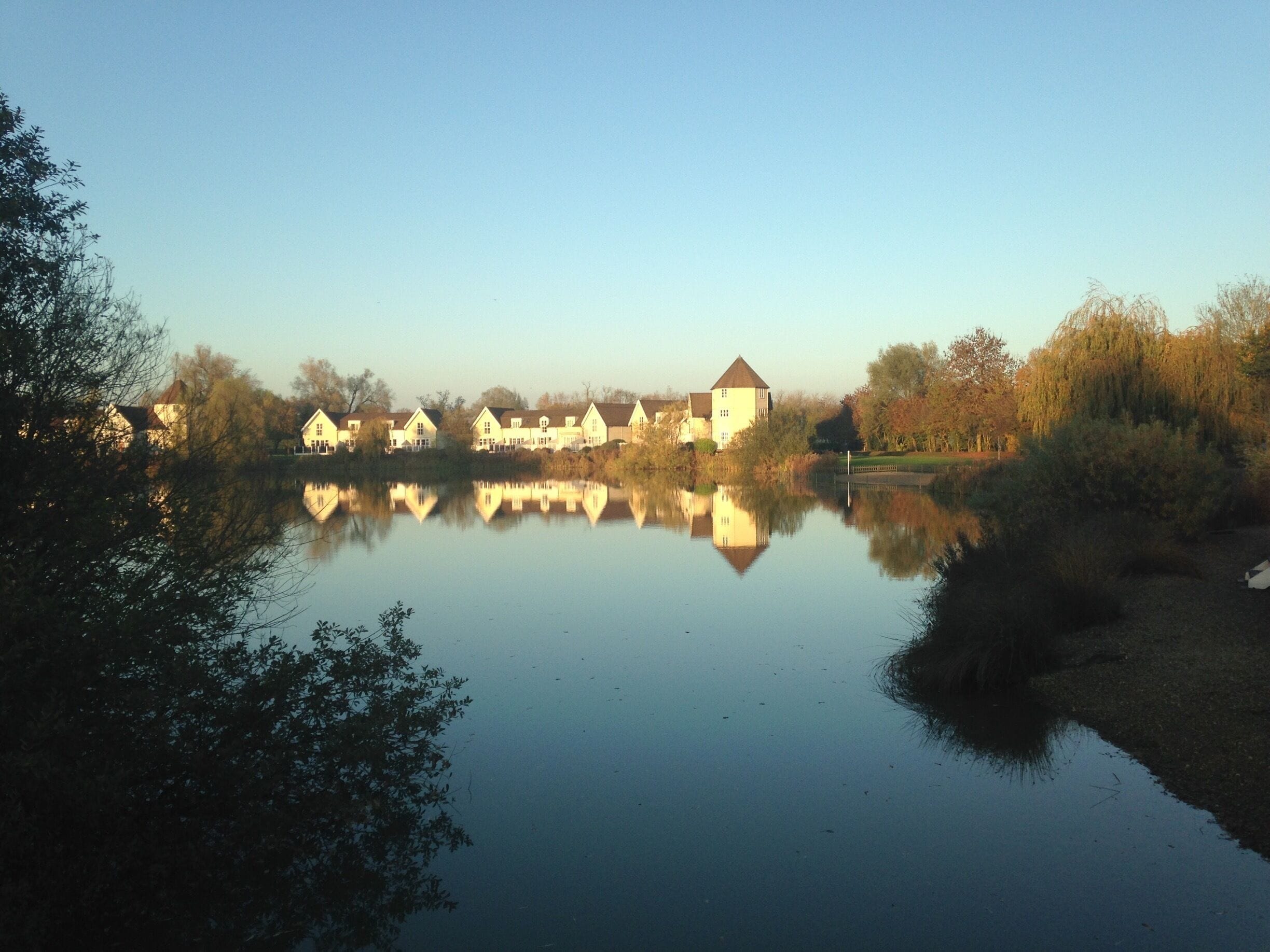 A calm lake reflecting houses and a tower.