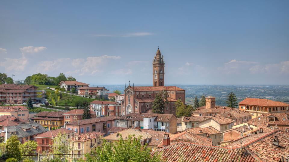 A town with a prominent church and tower, surrounded by terracotta-roofed buildings and lush greenery.
