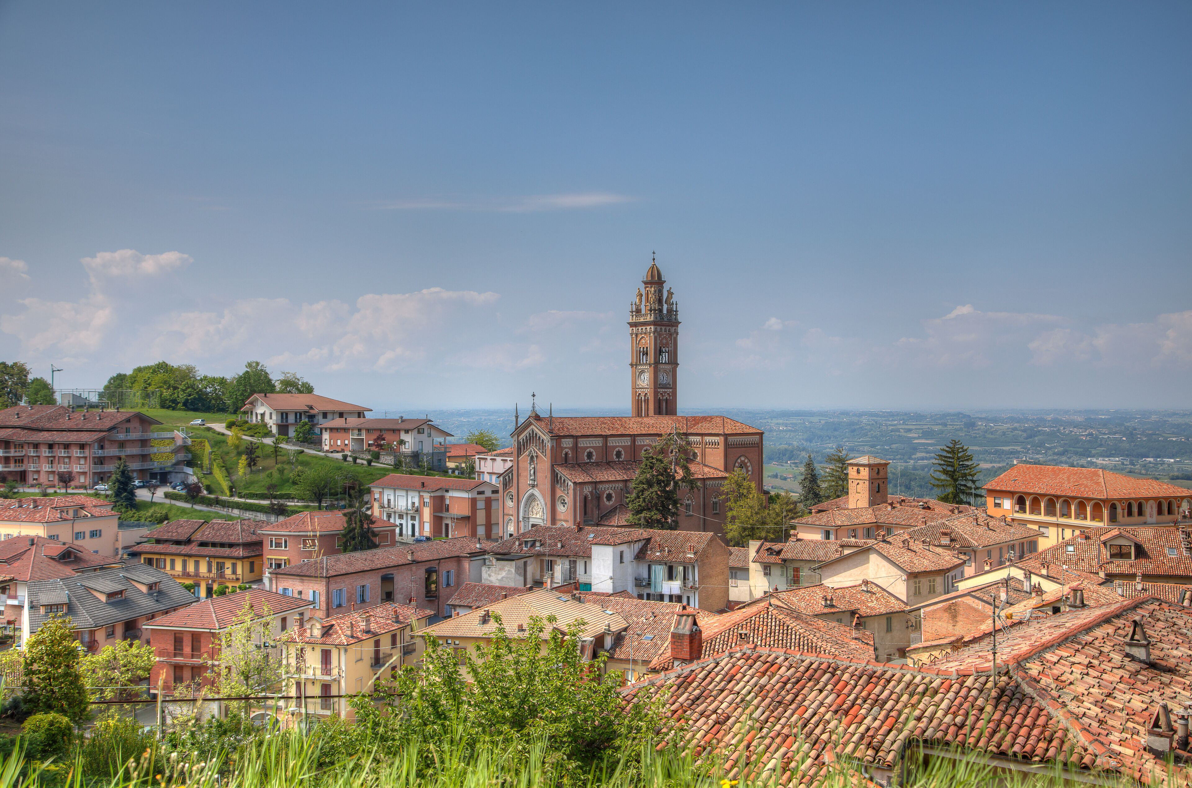A town with a prominent church and tower, surrounded by terracotta-roofed buildings and lush greenery.