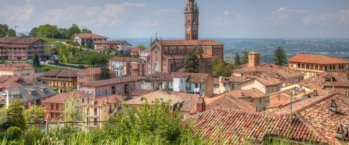 A town with a prominent church and tower, surrounded by terracotta-roofed buildings and lush greenery.