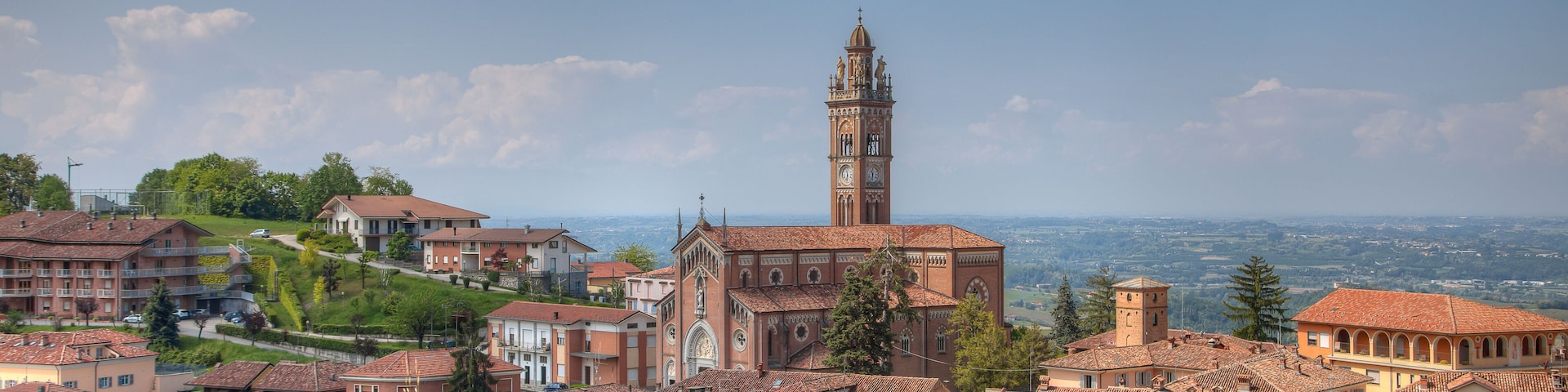 A town with a prominent church and tower, surrounded by terracotta-roofed buildings and lush greenery.