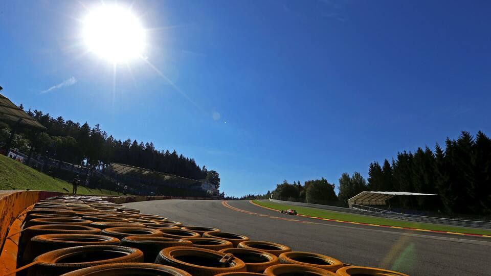 A race track with a car on the curve, surrounded by trees and a clear sky.