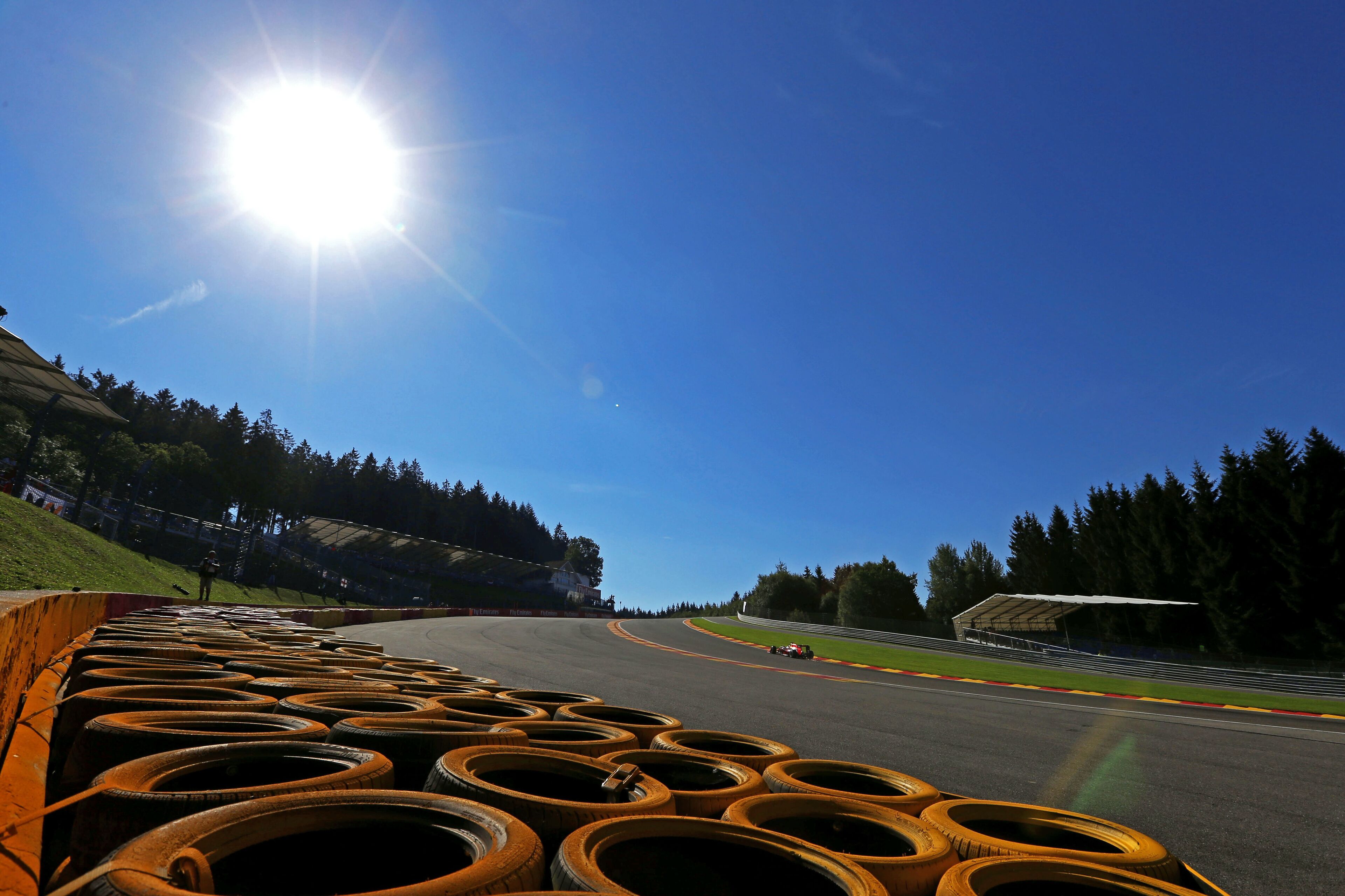 A race track with a car on the curve, surrounded by trees and a clear sky.