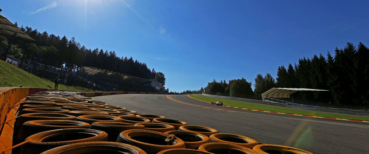 A race track with a car on the curve, surrounded by trees and a clear sky.