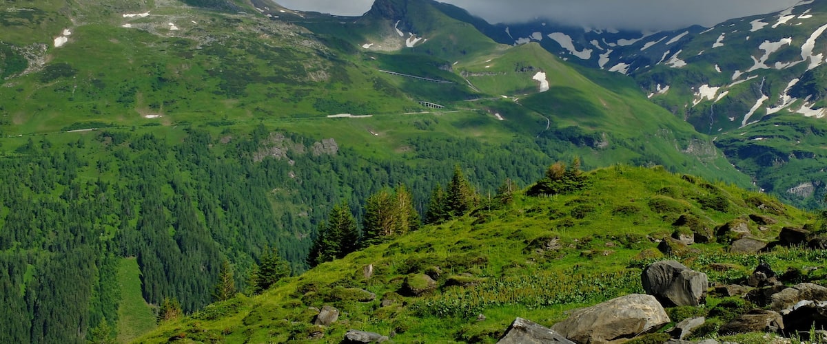 A mountainous landscape with dense forests, rocky outcrops, and a winding road.