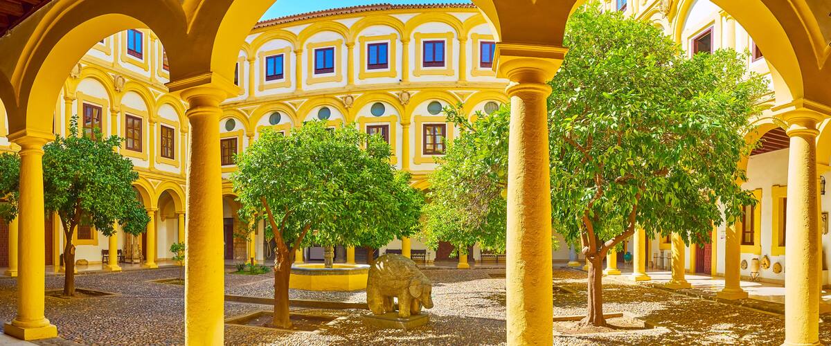 A courtyard with yellow buildings, arches, and trees.