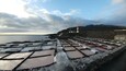 Kystlandskab med et fyrtårn, terrasserede saltbassiner og en stenvæg.