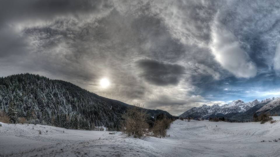 A snowy mountain landscape with a forested slope and a clear sky.