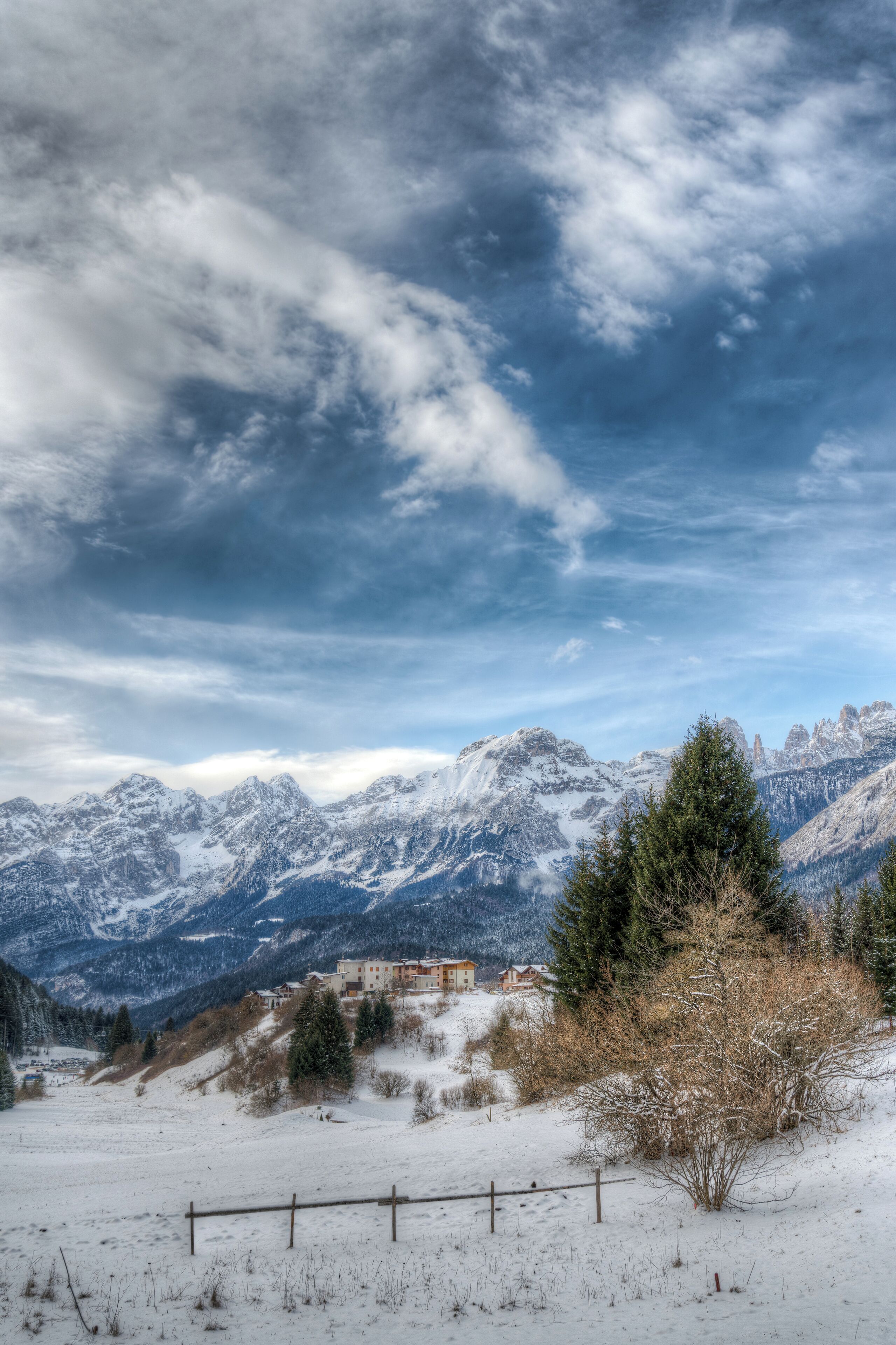 A snow-covered mountain landscape with a clear sky and a small building in the valley.
