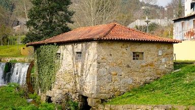 Uma casa de pedra com telhado de telhas, uma cascata e uma encosta verdejante.