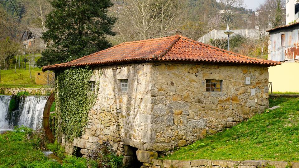 A stone house with a tiled roof, a waterfall, and a lush green hillside.