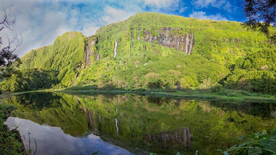 A mountain with a waterfall and a calm lake reflecting the greenery.