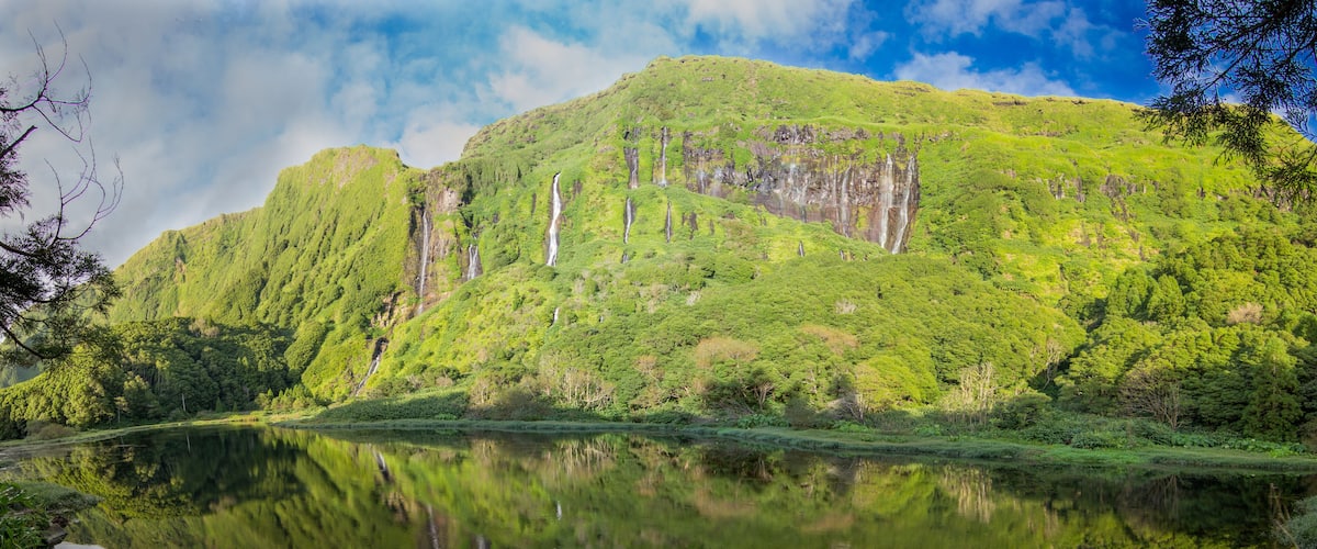 A mountain with a waterfall and a calm lake reflecting the greenery.